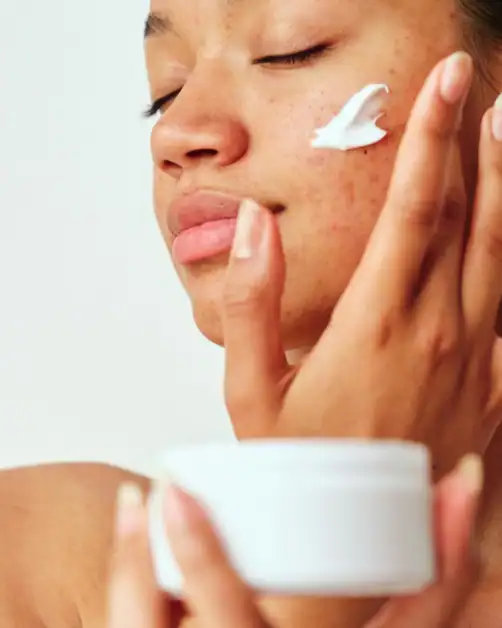 Woman applying face moisturizer on her face from a cream jar