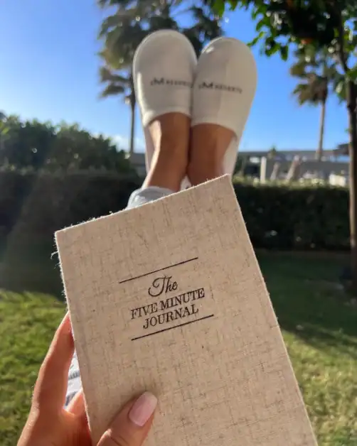 Woman holding five minute journal in hand in the morning as part of self-care routine