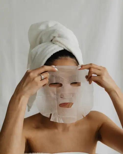 Woman applying face sheet mask as a part of self-care routine