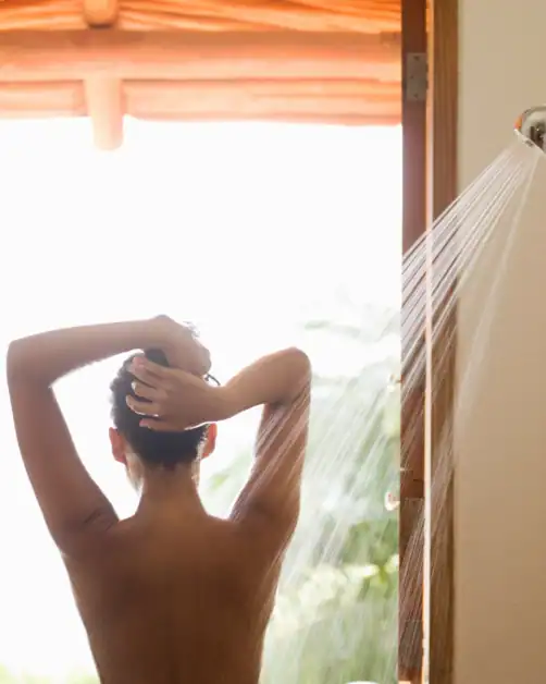 Woman rinsing her hair under a shower as part of a cold shower wellness habit