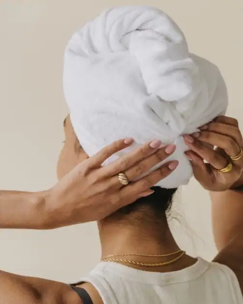 Woman with hair wrapped in a white towel adjusting it after washing her hair as part of a wellness routine